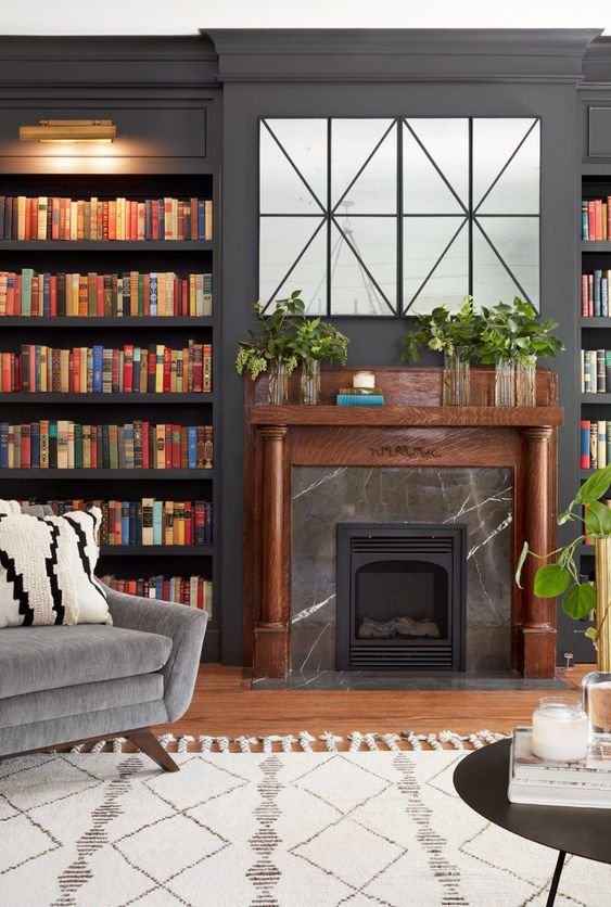 An elegant modern living room with graphite grey walls, built-in bookshelves, a fireplace clad with black marble and a TV hidden behind panels.
