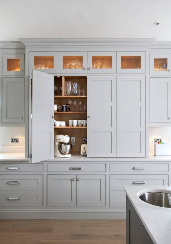 A dove grey contemporary kitchen with small appliances hidden in a cabinet with bi-fold doors to make the look sleek.