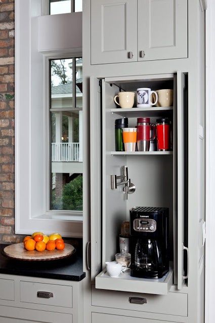 A small and narrow kitchen cabinet turned into a home coffee bar with a coffee maker on a retractable shelf and with lots of mugs.