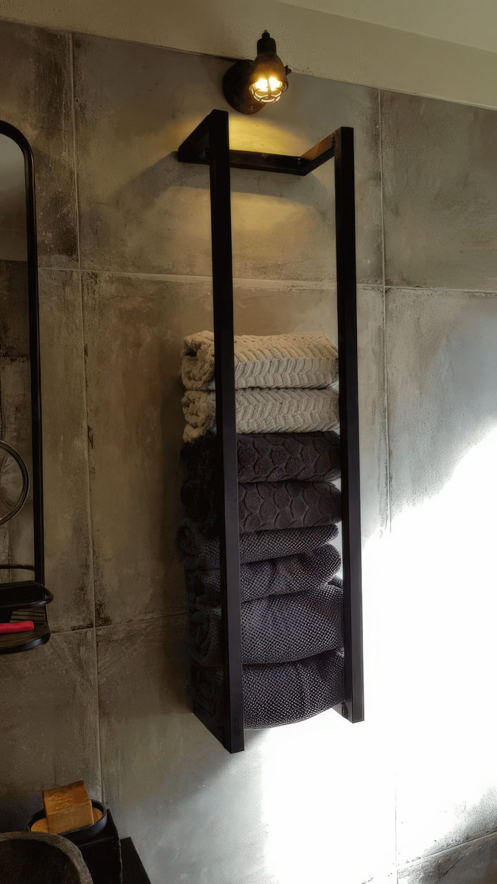 An industrial black metal wall-mounted shelf with various towels and a light over it is a stylish idea to store stuff.