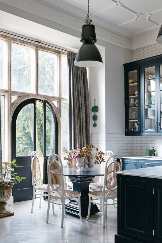 An elegant kitchen eat-in space right in the center, with a vintage dark wood table and airy rattan chairs.