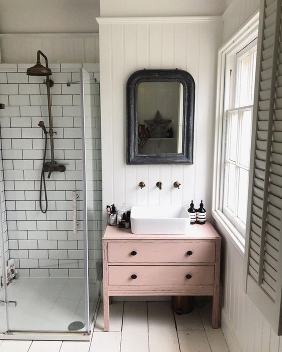 A dusty pink sink console table adds a touch of color and interest to the neutral bathroom.