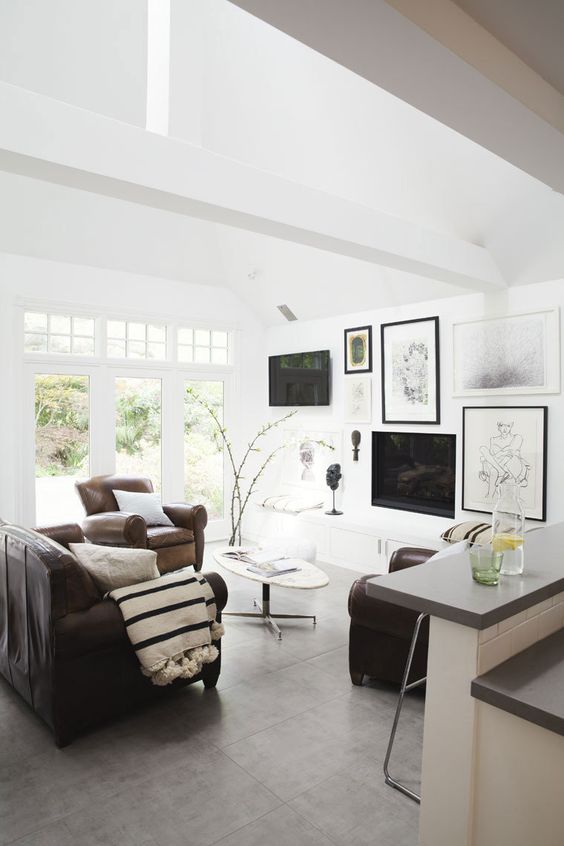 A modern neutral living room with brown leather furniture and a pretty black and white gallery wall that comprises a TV and a fireplace.