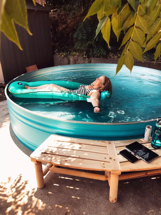 A blue stock tank pool with a wooden bench that doubles as a deck placed in the shadow is a cool idea.