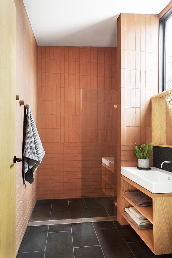 A bright bathroom with orange and yellow walls, black tiles on the floor, a stained vanity and white appliances.