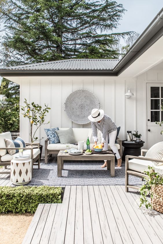 A cozy Scandinavian terrace with simple wooden furniture, white upholstery, a lemon tree and striped pillows.