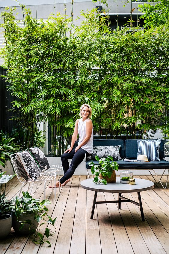 A fresh monochromatic terrace with a wooden deck, a greenery wall, greenery in pots and black and white furniture.