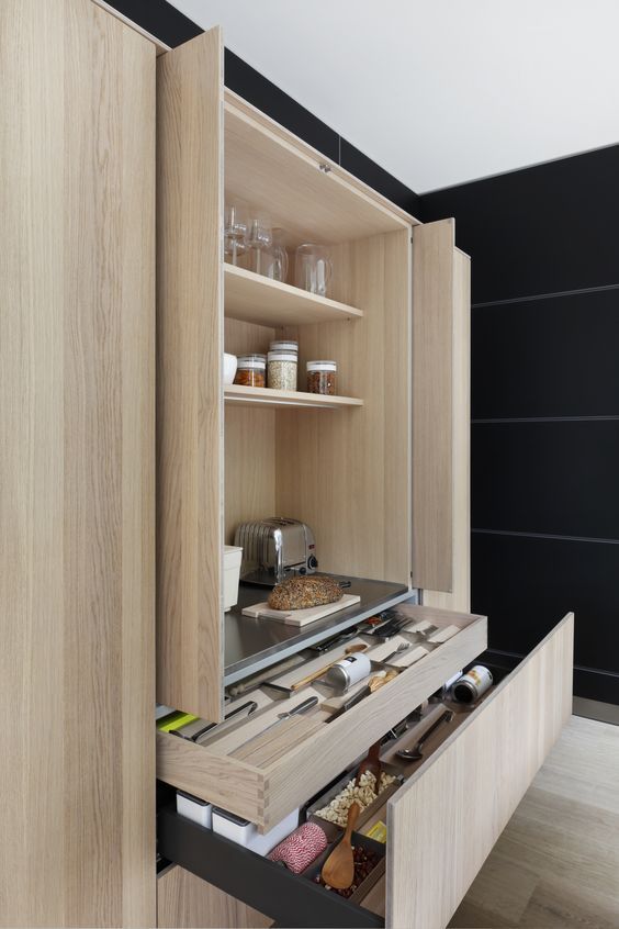 A light stained cabinet with pocket doors with appliances and spices inside plus necessary stuff in the drawers below.