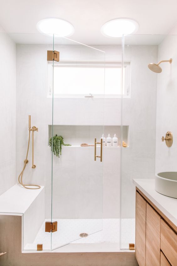 A lovely neutral bathroom with white walls, a stained vanity, a bench and a niche in the shower, gold fixtures.