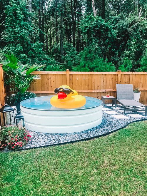 A lovely outdoor space with a green lawn, some blooms and plants, a stock tank pool, loungers and side tables, lanterns.