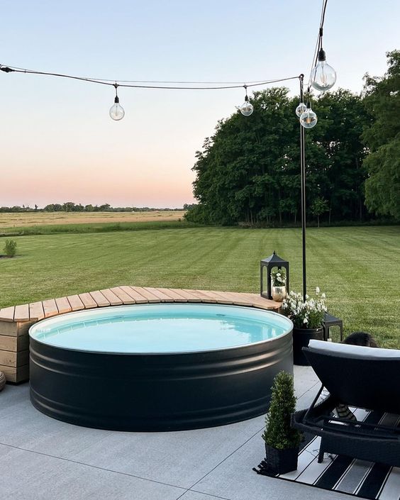 A minimal outdoor space with a tile clad deck, a black stock tank pool, loungers, rugs and a wooden bench next to the pool.