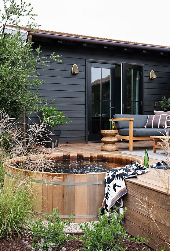 A Scandinavian backyard with a wooden deck and a stock tank covered with the same wood, with elegant and cozy furniture.