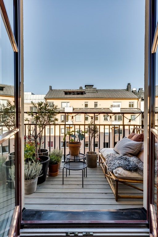 A simple and natural balcony with a rattan sofa, lots of pillows and blankets, potted greenery and other plants.