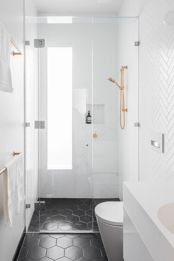 A tiny black and white bathroom with white herringbone tiles on the walls, black hexagon ones on the floor and gold fixtures.