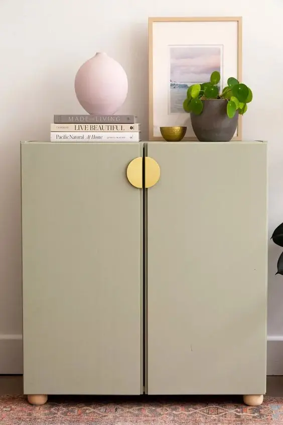 An IKEA Metod done with green paint and chic gold knobs and wooden legs, with books, decor and a potted plant.