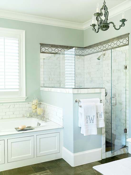 A light blue bathroom with a shower space clad with tiles, light blue walls and a half wall, a bathtub clad with panels.