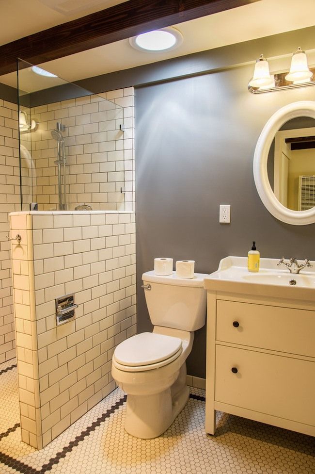 An elegant bathroom with grey walls, a neutrla shower space clad with white subway tiles, white furniture and appliances.