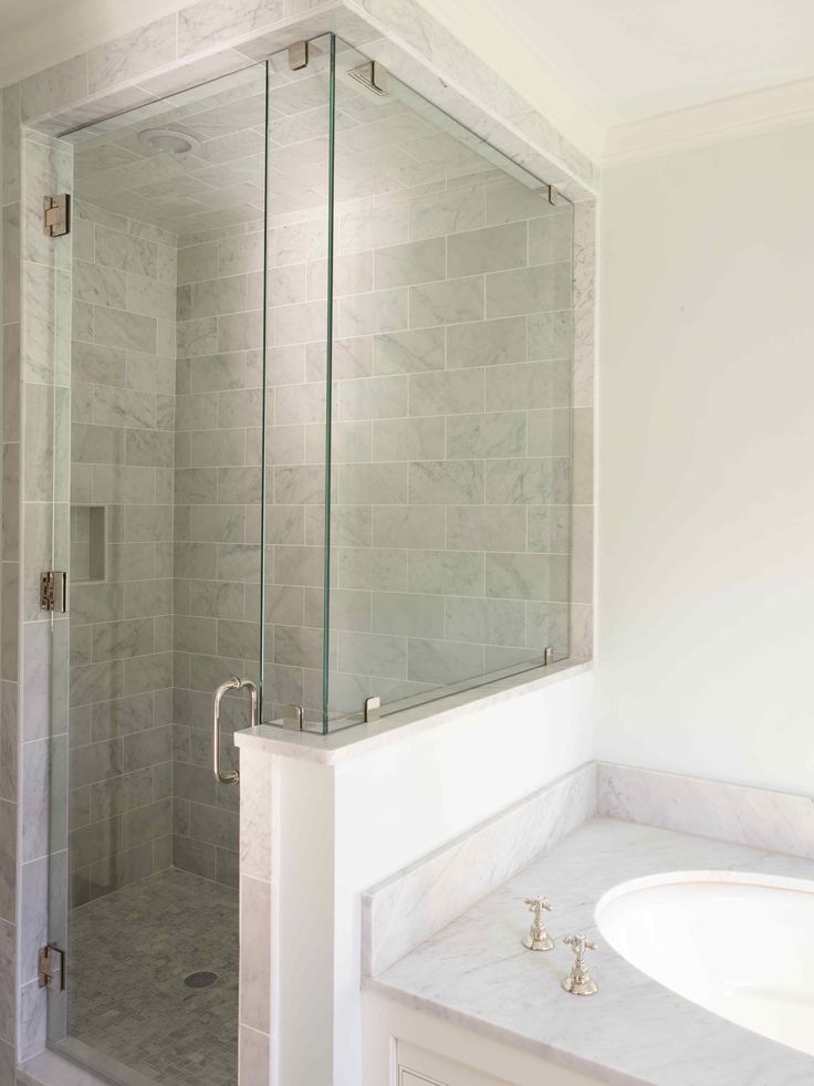 A neutral bathroom with a small shower space clad with tiles, a pony wall and a glass partition, a built-in sink in the vanity.