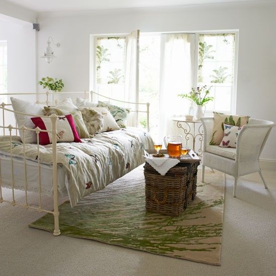 A chic vintage summer living room with floral rpint textiles, a green print rug and lots of greenery in pots and vases.