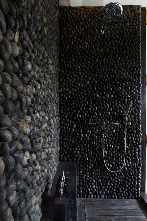 A beautiful and refined shower clad with black pebble,s with a wooden floor and a black stone console is a dramatic and chic idea.
