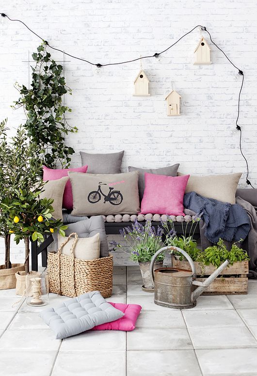 A bright and fun summer terrace with a black bench, colorful pillows, pallets and boxes with greenery and blooms, a garland and birdhouses for decor.
