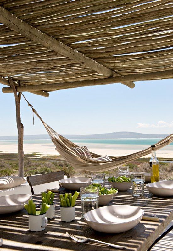 A cheerful island summer terrace made of wood, with neutral textiles and a cool dining zone plus a gorgeous sea view.