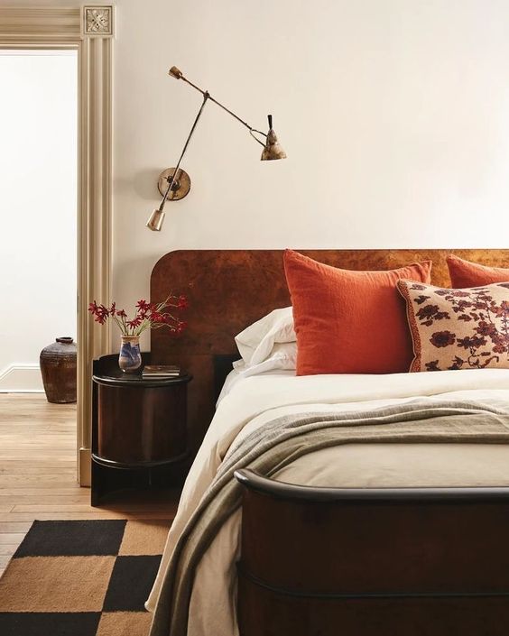 The refined bedroom is done with a dark-stained bed and a rust velvet headboard, a dark round nightstnad and a cool sconce.