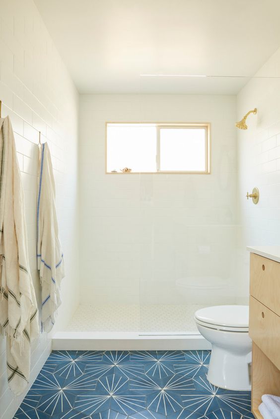 White tiles on the walls and ceilings, navy tiles on the floor, a light-colored wooden vanity and a small window is inviting.